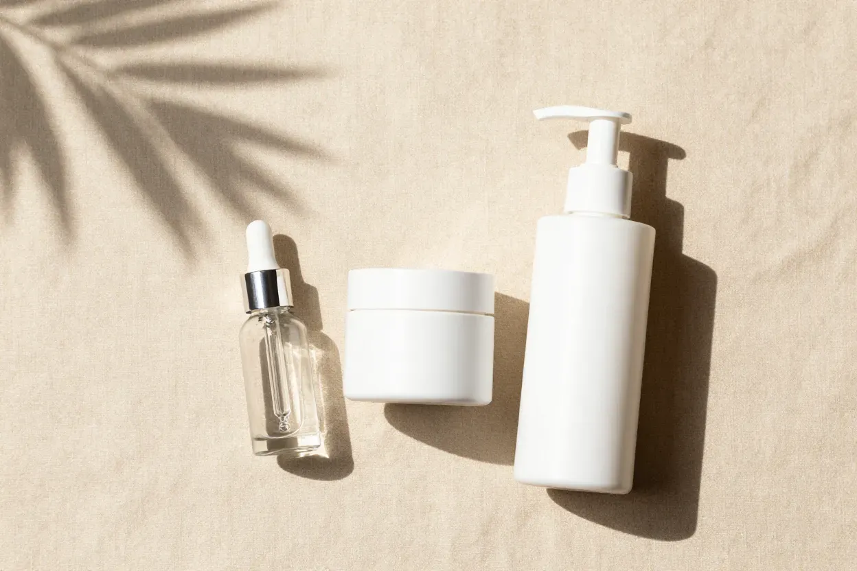 Serum, moisturiser and cleanser laid out on linen in soft tropical light